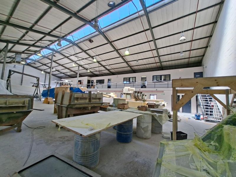 Spacious industrial warehouse featuring high exposed steel truss ceilings with integrated skylights, concrete flooring, and a functional mezzanine level.