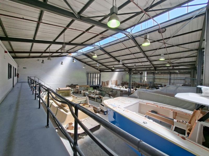 Spacious industrial workshop featuring a high-clearance steel truss roof with integrated skylights and a mezzanine level walkway overlooking the main floor area.