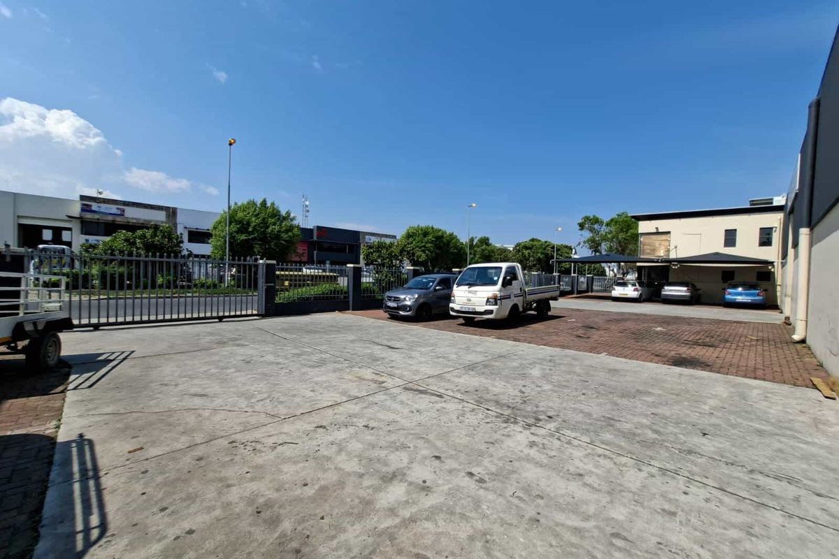 Spacious industrial yard area featuring a combination of concrete and brick paving, secure perimeter fencing, and covered parking bays.