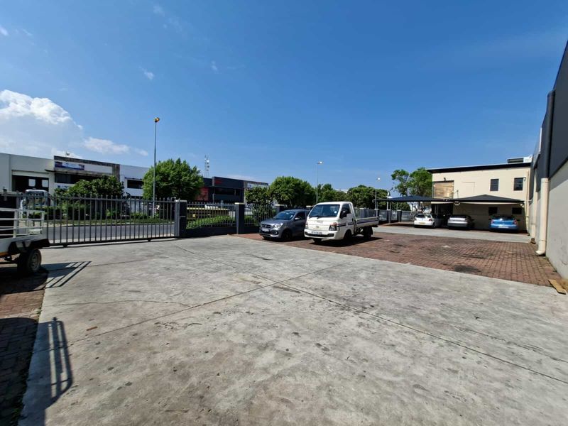 Spacious industrial yard area featuring a combination of concrete and brick paving, secure perimeter fencing, and covered parking bays.