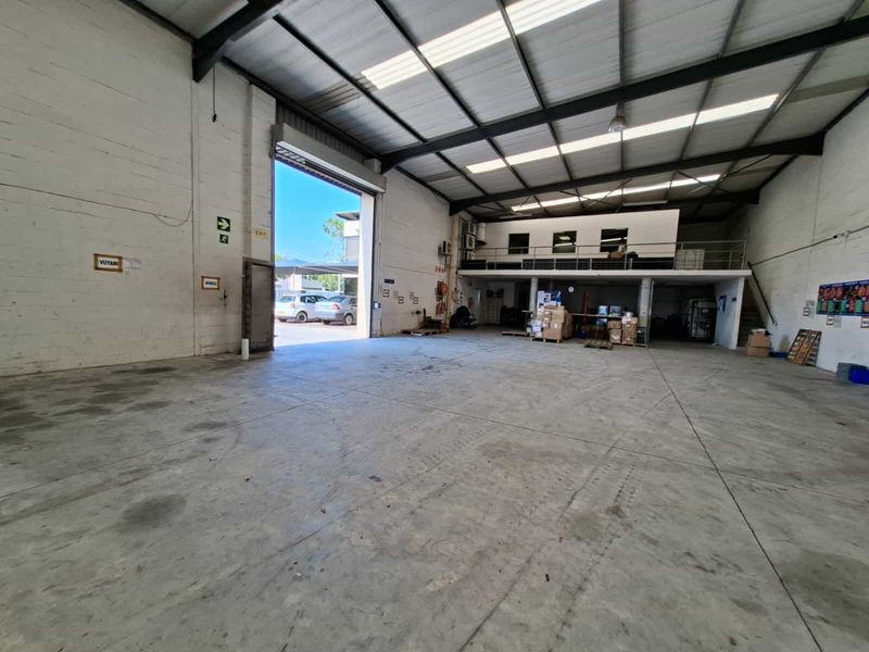 Spacious industrial warehouse unit featuring high ceilings with exposed steel trusses, a mezzanine level, and a large roller shutter door for vehicle access.