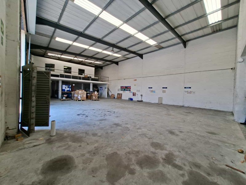 Spacious industrial warehouse unit featuring high ceilings with skylights, concrete flooring, and a mezzanine level, suitable for storage or light manufacturing operations.