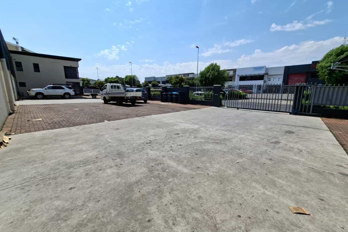 A spacious industrial rear yard featuring concrete and brick paving, enclosed by secure metal fencing and gates.