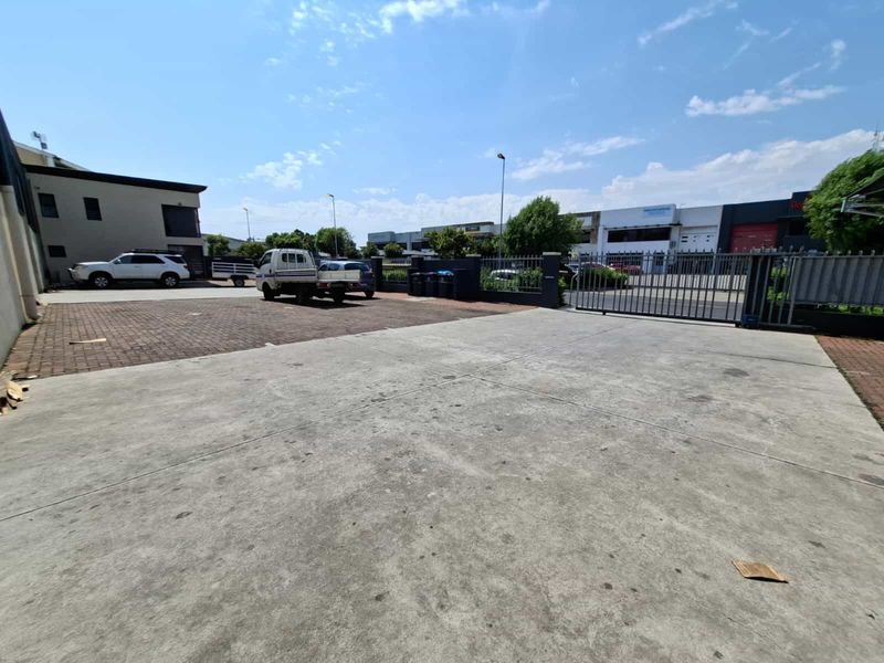 A spacious industrial rear yard featuring concrete and brick paving, enclosed by secure metal fencing and gates.