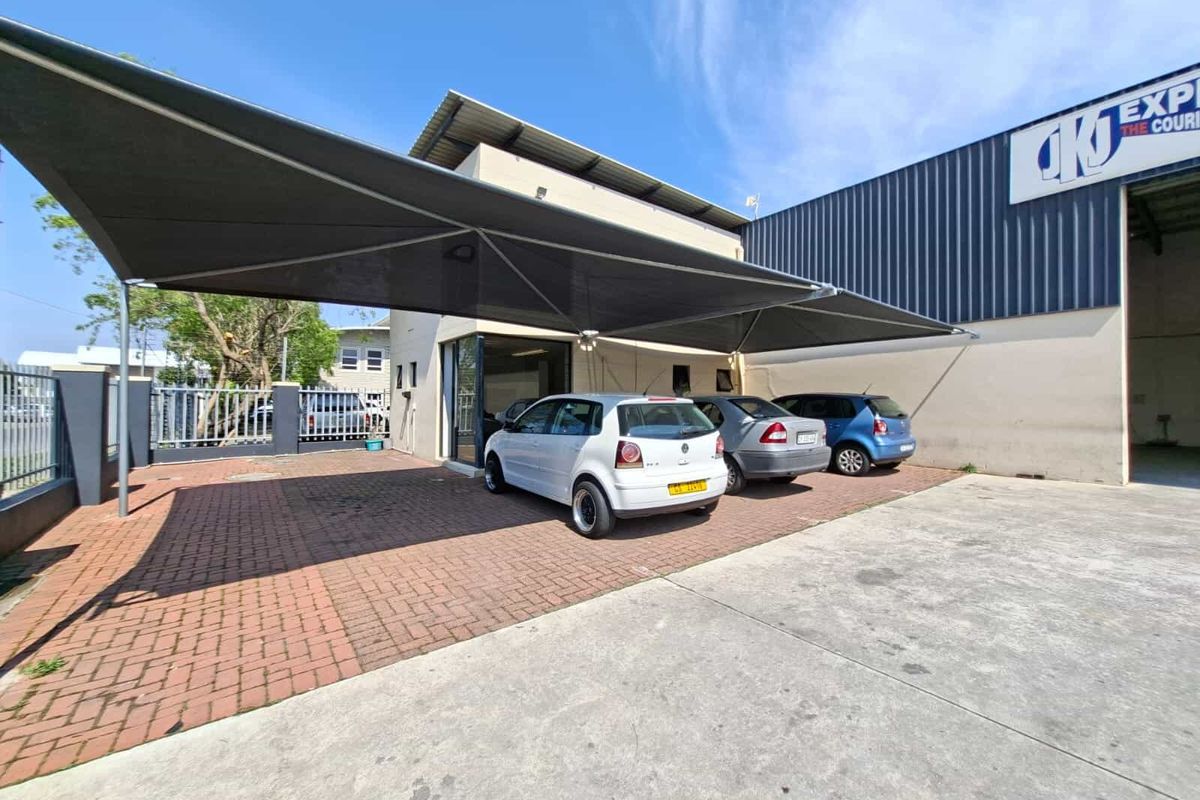 Industrial property exterior featuring a paved parking area with a large shade sail structure and metal cladding facade.