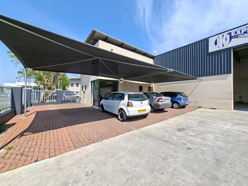 Industrial property exterior featuring a paved parking area with a large shade sail structure and metal cladding facade.