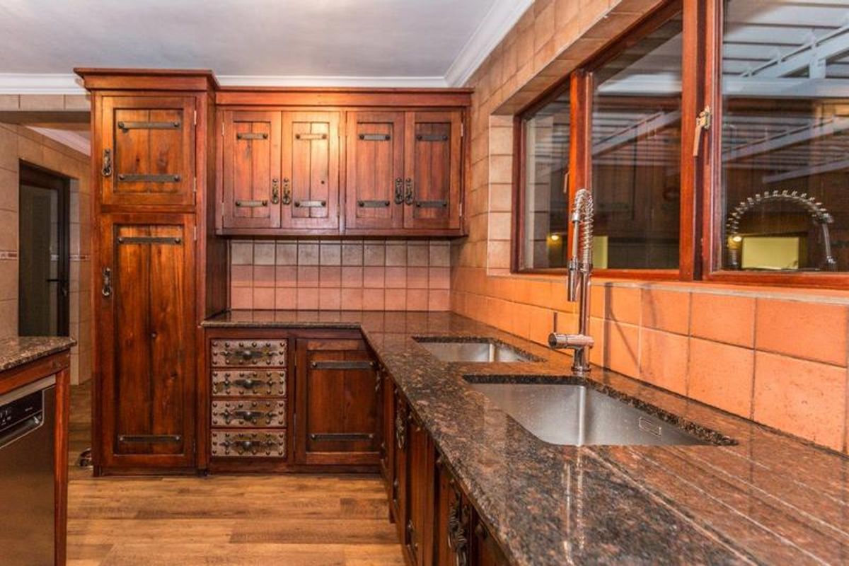 A rustic-style kitchen featuring dark wood cabinetry, granite countertops, a double stainless steel sink, and a tiled backsplash.