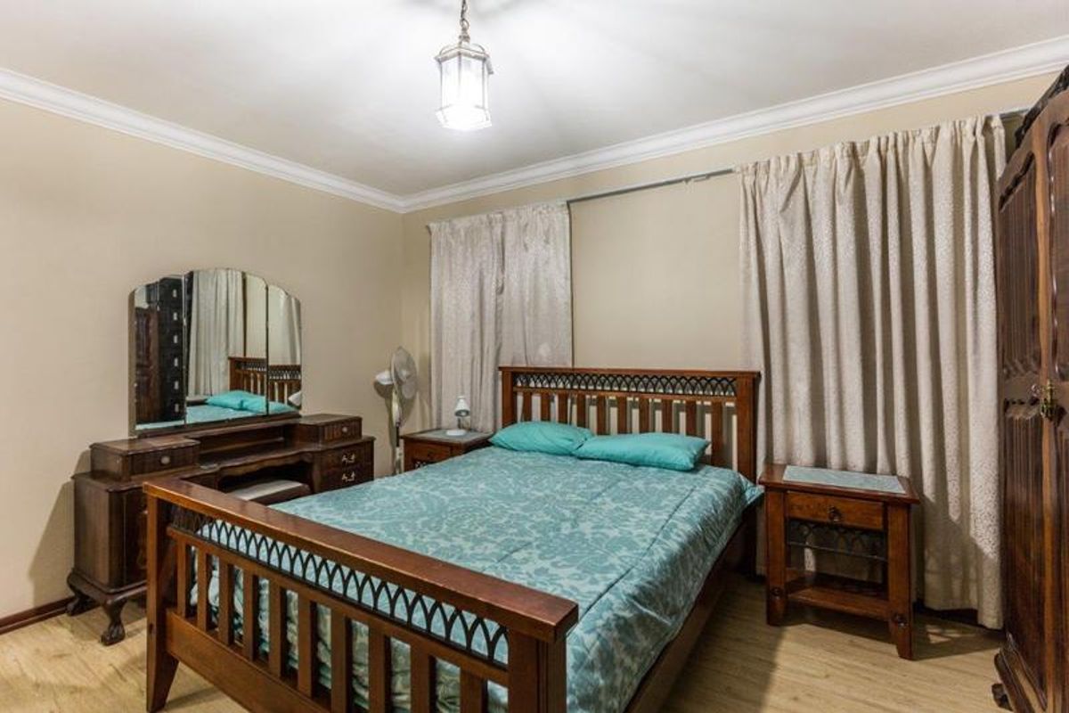 A well-maintained bedroom featuring laminate flooring, decorative coving, and a central pendant light fixture.