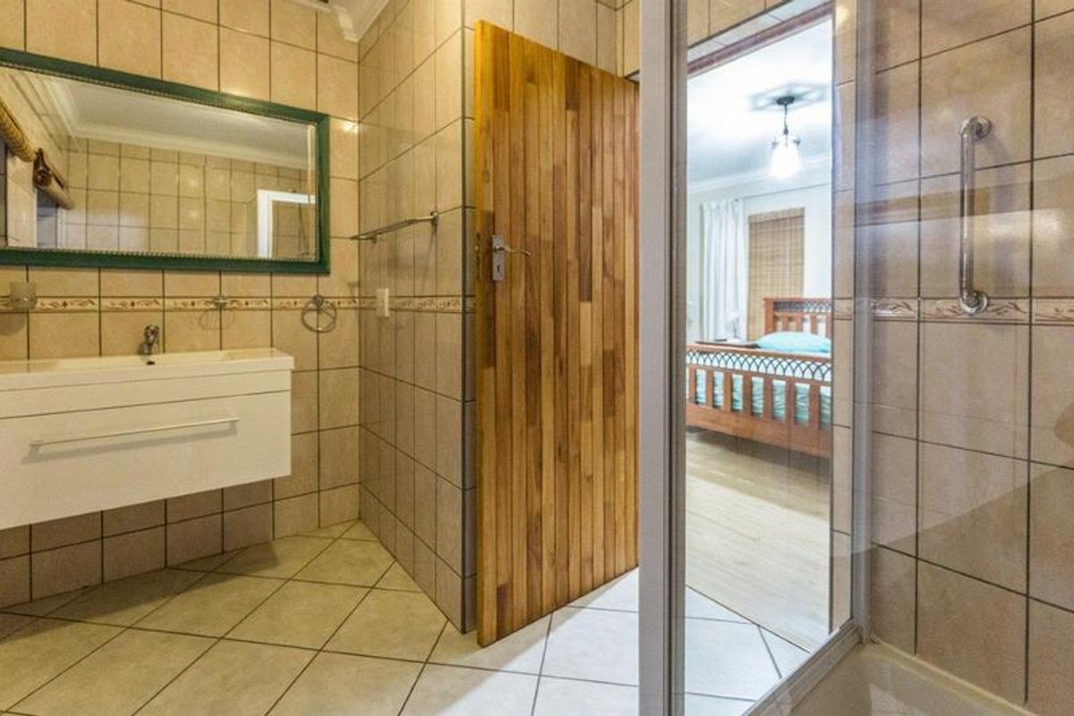 A functional bathroom featuring a wall-mounted vanity, tiled surfaces, and a glass-enclosed shower, with direct access to an adjacent bedroom.