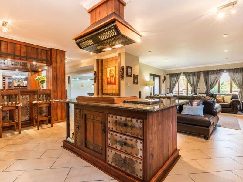 Spacious open-plan living area featuring a rustic wooden kitchen island with granite countertop, built-in bar, and tiled flooring throughout.