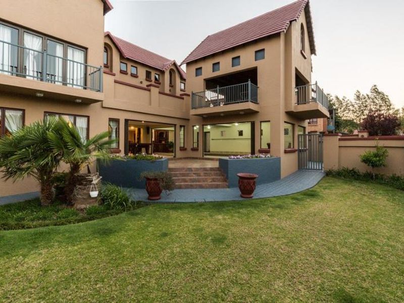 Rear view of a multi-story house featuring a tiled roof, balconies, sliding doors leading to a paved patio, and a well-maintained garden.