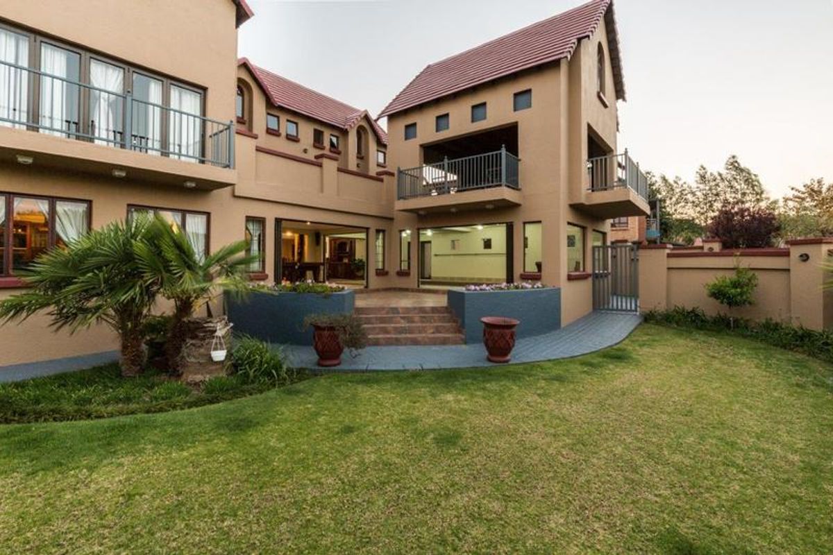 Rear view of a multi-story house featuring a tiled roof, balconies, sliding doors leading to a paved patio, and a well-maintained garden.