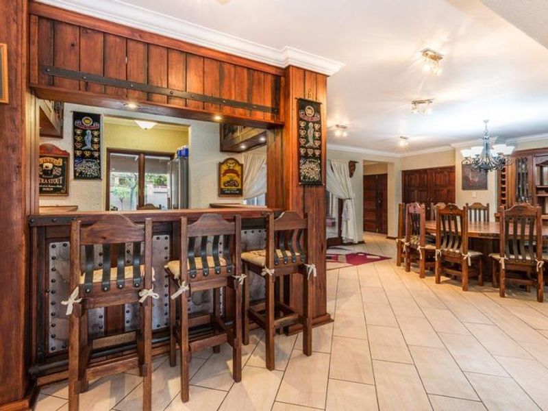 Spacious open-plan area featuring a custom built-in wooden bar, tiled flooring, and elegant dining space with integrated cabinetry and warm lighting.