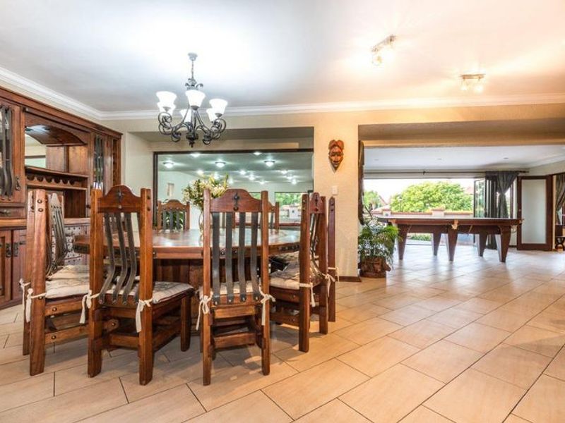 Spacious dining area featuring built-in wooden cabinetry, tiled flooring, and an open-plan layout connecting to an adjacent entertainment space.