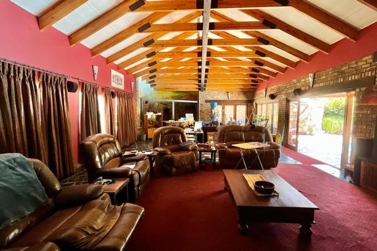 Spacious living area featuring high exposed timber roof trusses, an exposed brick wall, a fireplace, and large sliding doors opening to the outdoors.
