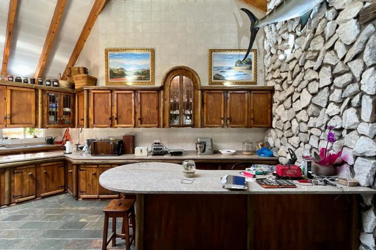 Rustic kitchen featuring exposed timber trusses, a prominent stone feature wall, slate flooring, and custom timber cabinetry with a stone-topped breakfast bar.