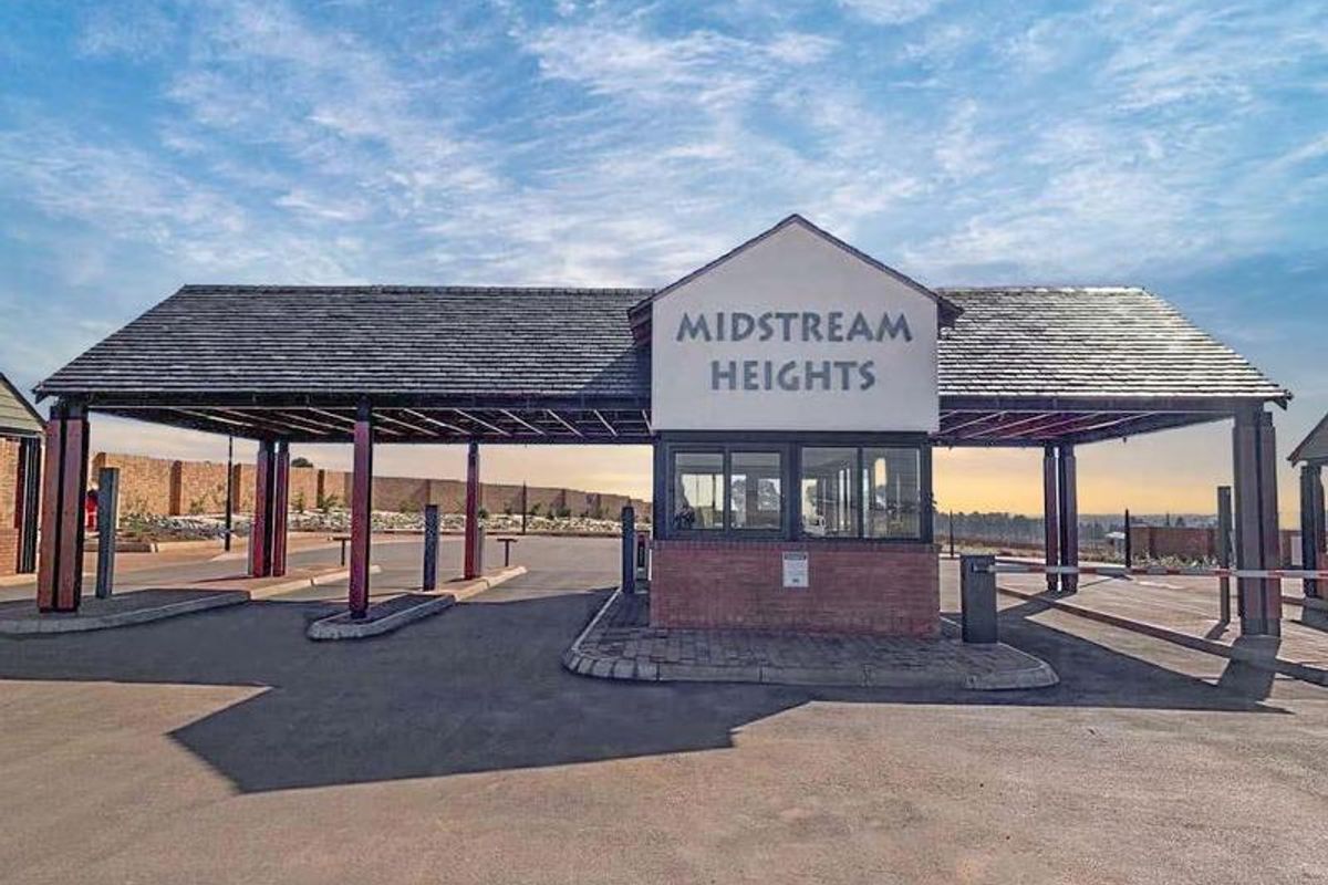 The main entrance gatehouse for Midstream Heights, featuring a secure guard station, asphalt driveway, and covered access point.