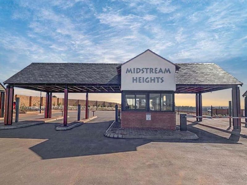 The main entrance gatehouse for Midstream Heights, featuring a secure guard station, asphalt driveway, and covered access point.