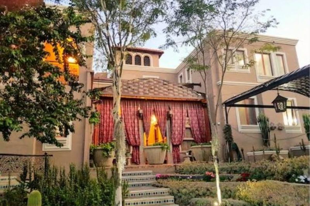 A rear exterior view of the guest house featuring a landscaped garden, stone steps leading to a covered terrace area with decorative curtains.