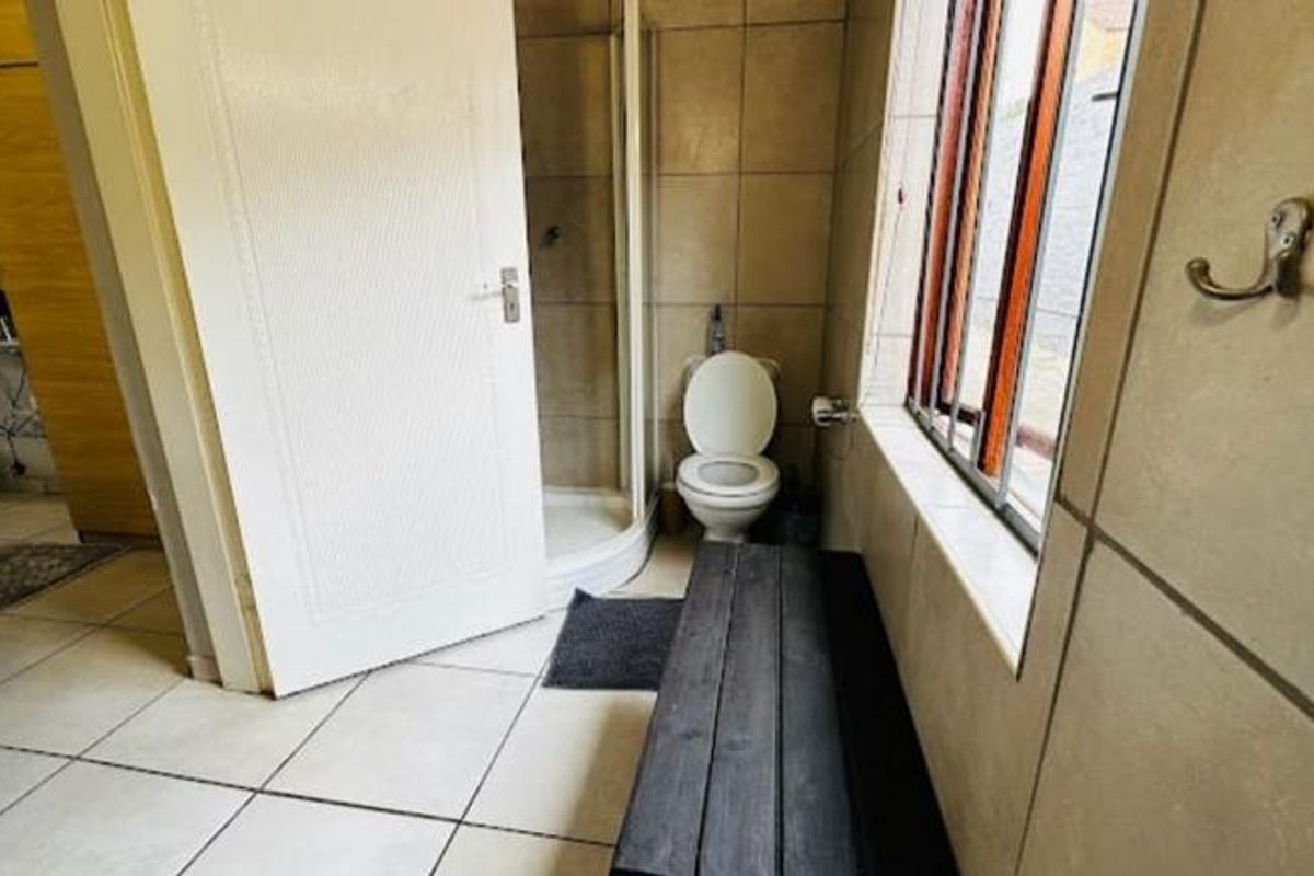 A functional bathroom featuring a shower enclosure, toilet, and tiled finishes, with natural light provided by a side window.