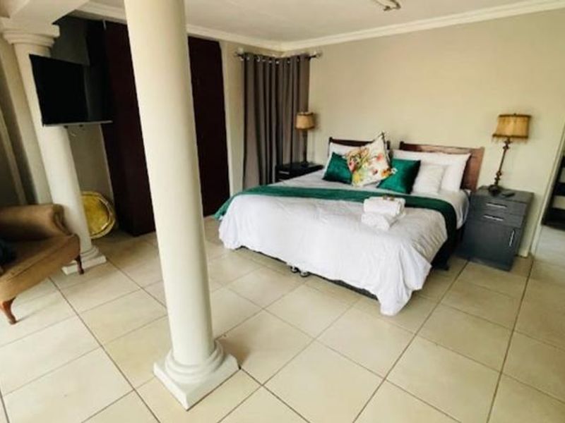 Spacious bedroom featuring tiled flooring, a structural column, and an en-suite bathroom entrance, offering a functional layout for guest accommodation.