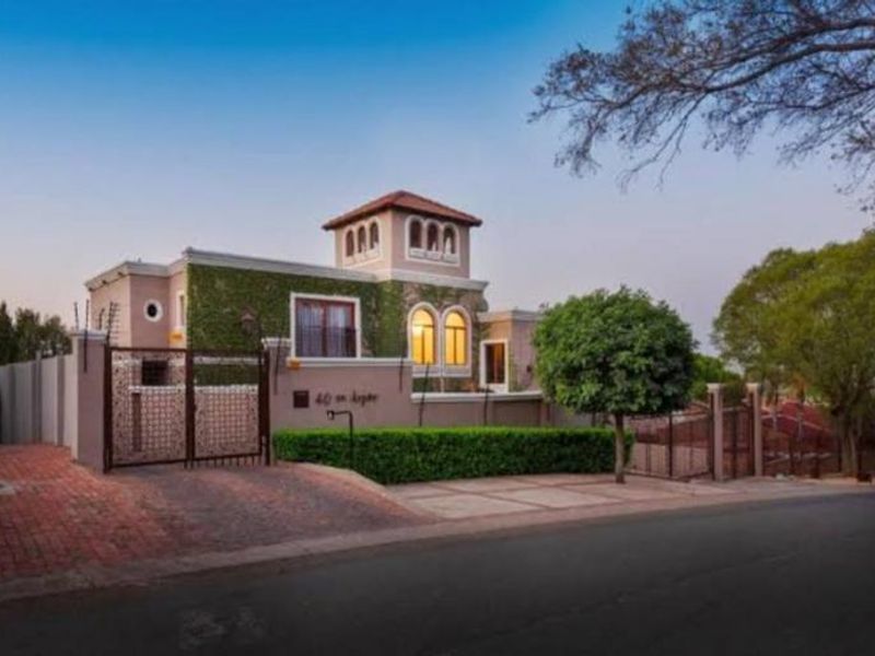 Front elevation of a guest house featuring a distinctive tower, arched windows, brick paved driveway, and secure perimeter wall with electric fencing.