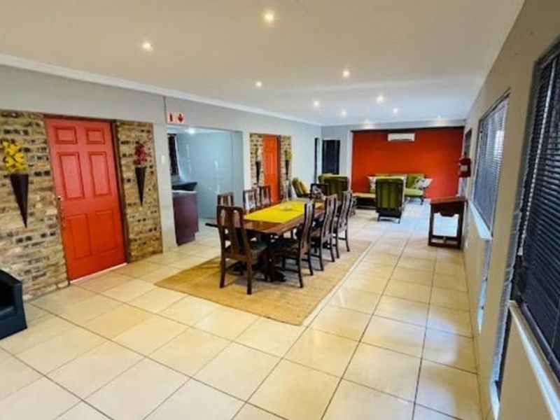 Spacious open-plan living and dining area featuring tiled floors, recessed lighting, and an exposed brick accent wall with a vibrant red entrance door.