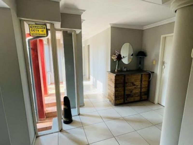A bright hallway featuring tiled flooring, decorative coving, and structural columns, providing access to adjacent areas of the guest house.