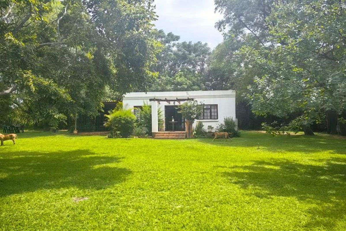 A rear view of the property featuring a white facade, a small pergola over the entrance, and a spacious, well-maintained garden lawn.