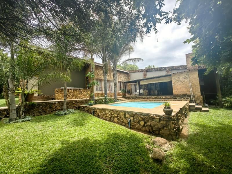 Outdoor entertainment area featuring a swimming pool, stone retaining walls, and a covered patio set within a mature garden.