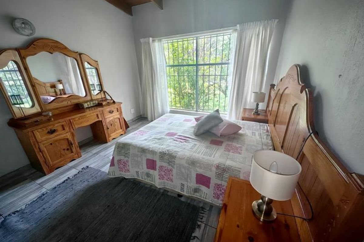 A bedroom featuring exposed timber ceiling beams, tiled flooring, and a large window with security bars overlooking the garden.
