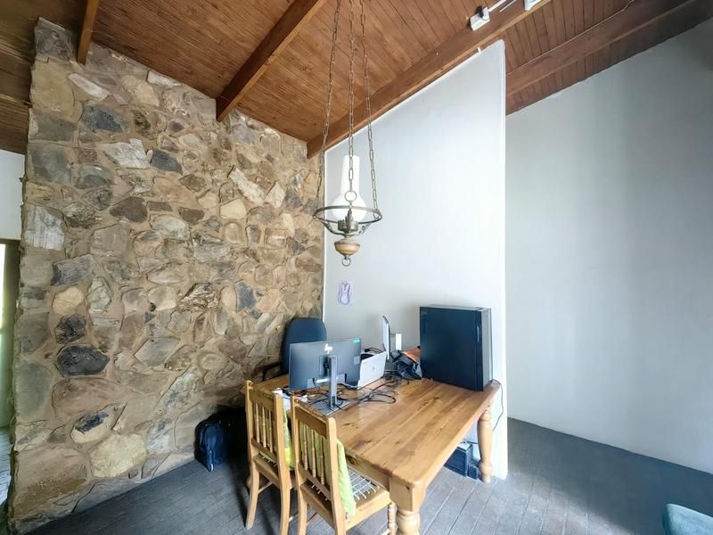 A home office space featuring a rustic exposed stone wall, high timber raked ceilings, and a classic pendant light fixture.