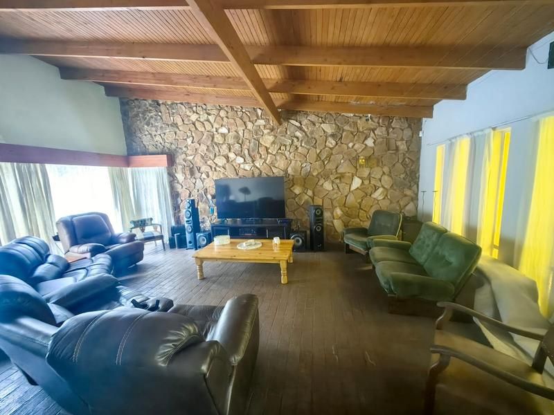 Spacious living room featuring a rustic stone feature wall, exposed timber beam ceiling, and dark timber flooring, creating a warm and character-filled atmosphere.