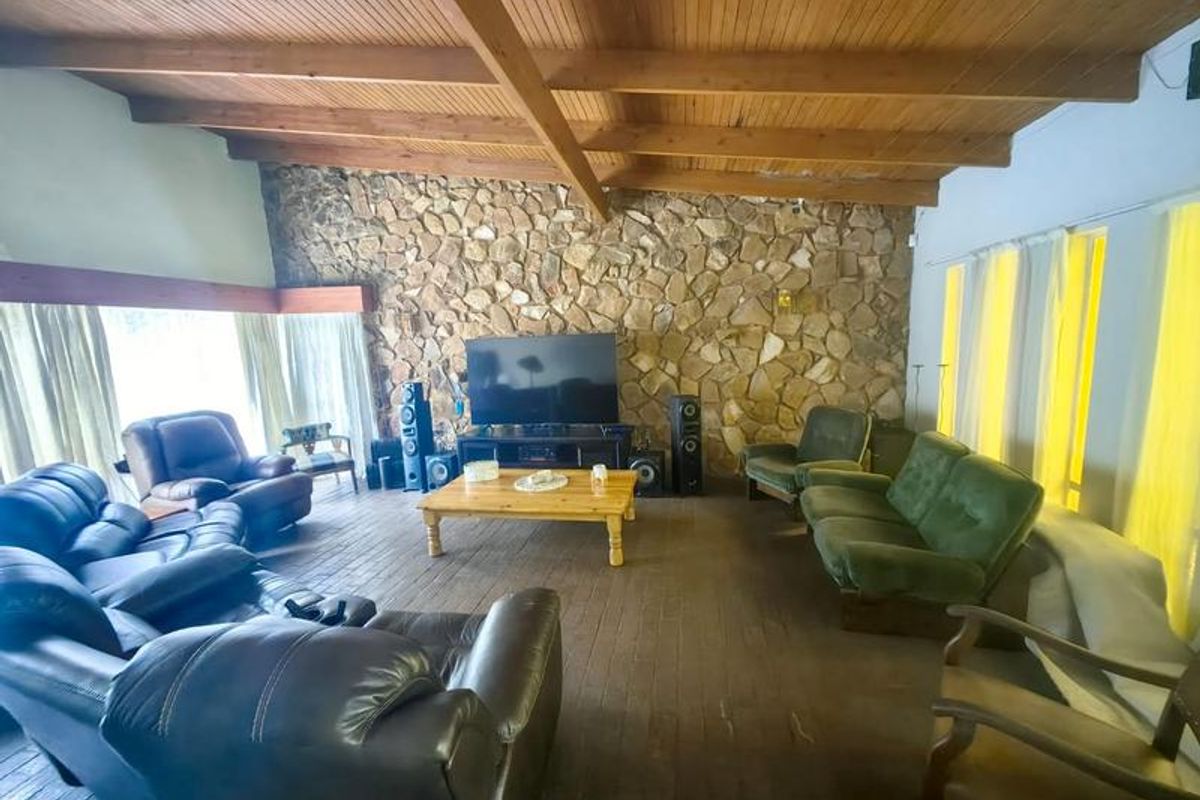 Spacious living room featuring a rustic stone feature wall, exposed timber beam ceiling, and dark timber flooring, creating a warm and character-filled atmosphere.