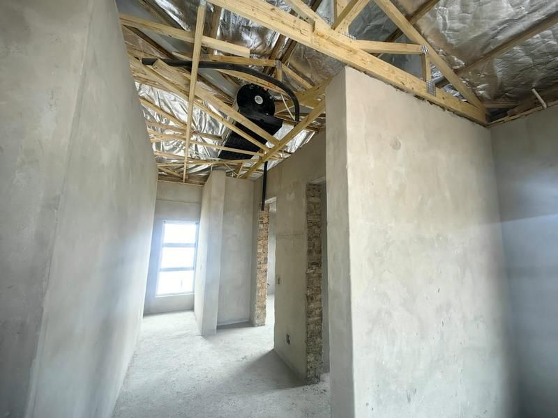 An unfinished interior space featuring exposed timber roof trusses, reflective insulation, and raw plastered masonry walls, currently in a shell construction state.