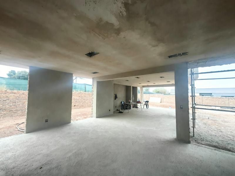 An expansive open-plan living area currently under construction, featuring raw plastered walls, concrete flooring, and recessed lighting points ready for final finishes.