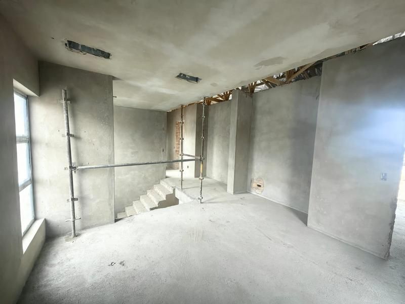 An unfinished interior space under construction featuring exposed concrete walls, a concrete staircase, and visible roof trusses, offering a blank canvas for renovation.