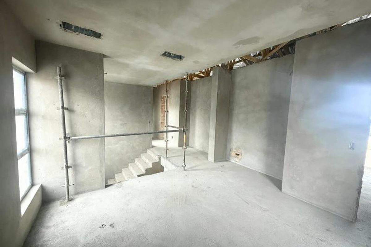 An unfinished interior space under construction featuring exposed concrete walls, a concrete staircase, and visible roof trusses, offering a blank canvas for renovation.