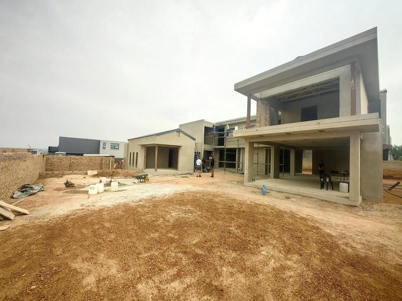 Rear view of a residential property currently under construction, featuring a large unlandscaped yard and unfinished structural exterior elements.