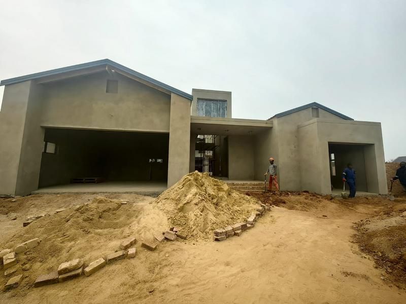 Front elevation of a house under construction, featuring a plastered facade, double garage, and covered entrance area with ongoing site works.