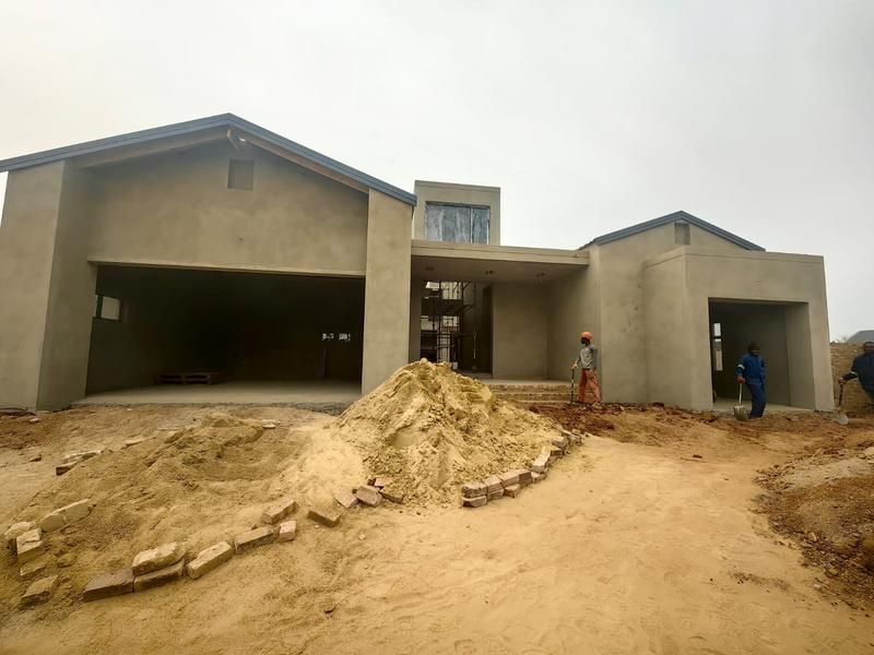 Front elevation of a residential property currently under construction, featuring a plastered facade, double garage, and covered entrance area.