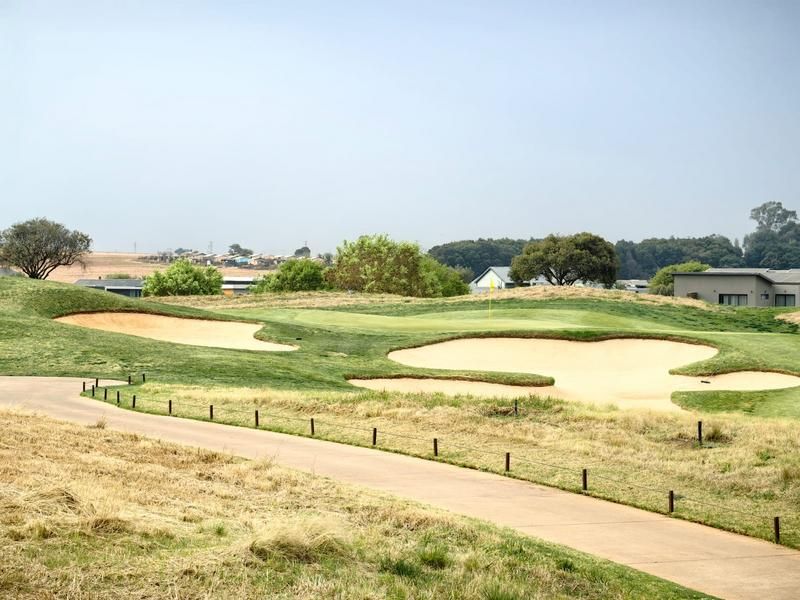 A scenic view overlooking a well-maintained golf course with sand bunkers and a paved cart path in the foreground.