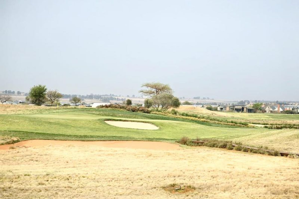 A scenic view overlooking a well-maintained golf course with sand bunkers and distant residential properties.