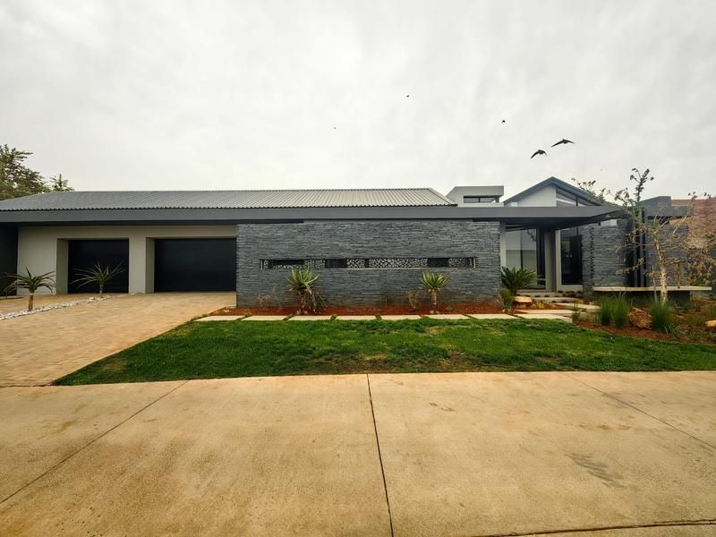 Modern single-story residence featuring a striking stone-clad facade, double garage, and a well-maintained front garden with paved driveway access.