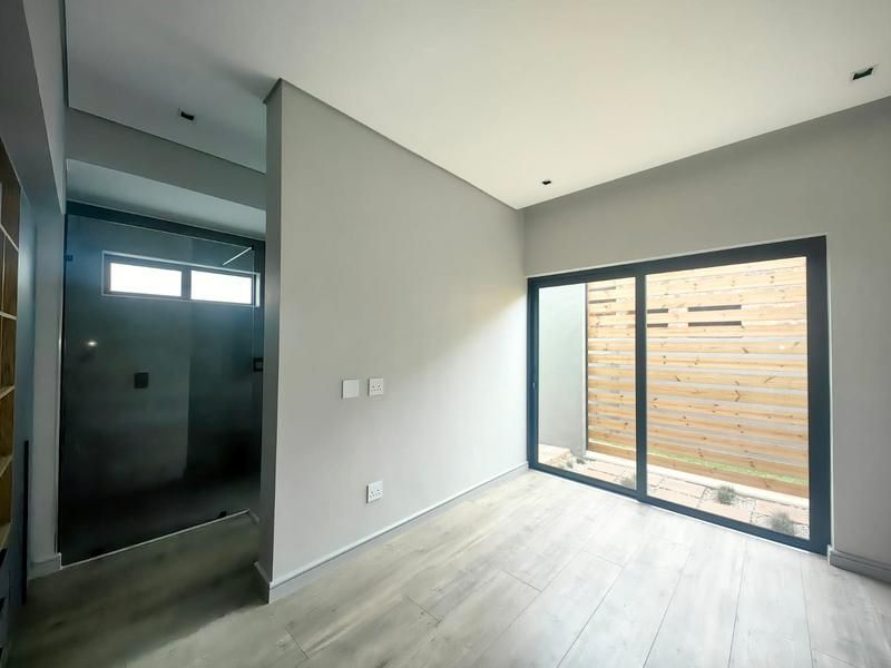 Modern bedroom featuring light laminate flooring, recessed lighting, and a sliding glass door opening to a private outdoor area with a timber privacy screen.