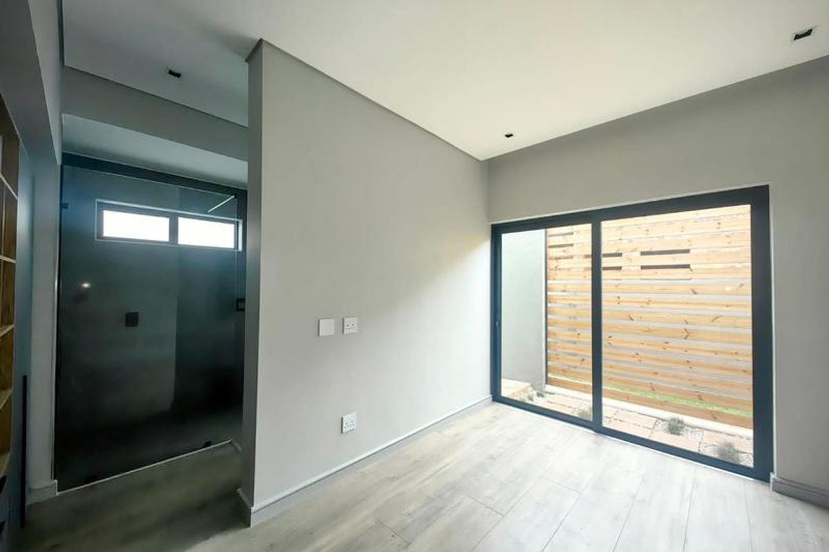 Modern bedroom featuring light laminate flooring, recessed lighting, and a sliding glass door opening to a private outdoor area with a timber privacy screen.