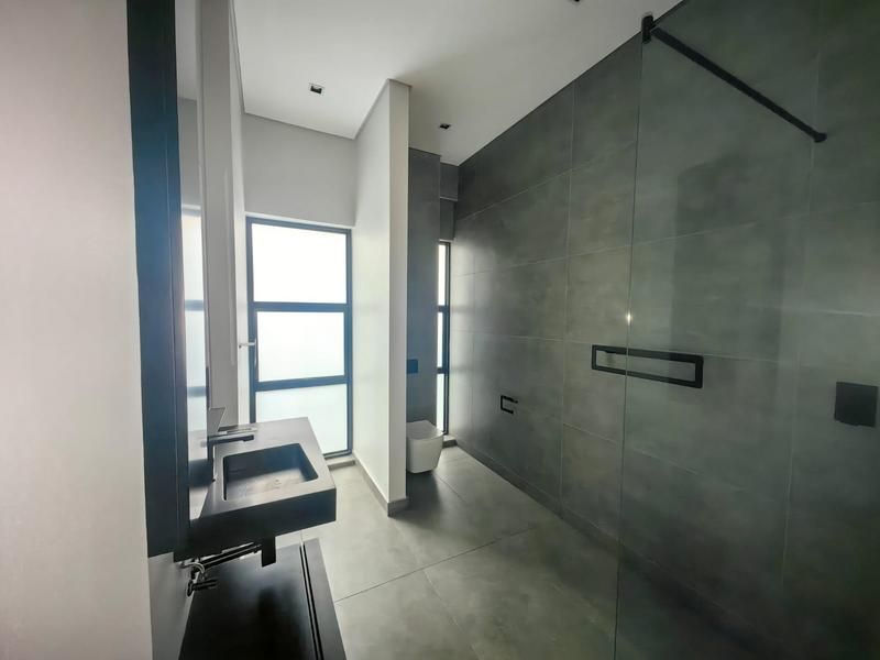 Modern bathroom featuring large format grey tiling, a walk-in glass shower, wall-mounted basin, and a wall-hung toilet with contemporary finishes.