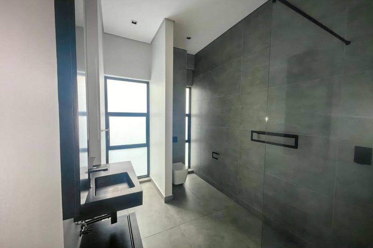 Modern bathroom featuring large format grey tiling, a walk-in glass shower, wall-mounted basin, and a wall-hung toilet with contemporary finishes.