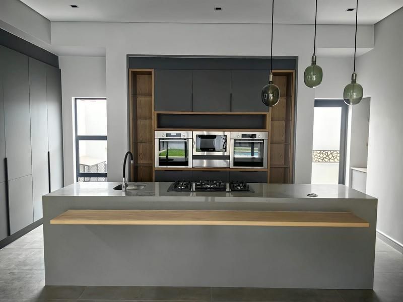 Modern kitchen featuring a large central island with stone countertop, integrated gas hob, built-in appliances, and sleek dark cabinetry with wood accents.