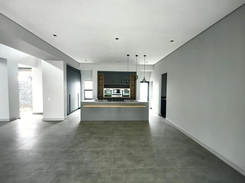 Modern, spacious kitchen featuring a central island, built-in ovens, sleek cabinetry, and large-format floor tiles in an open-plan layout.